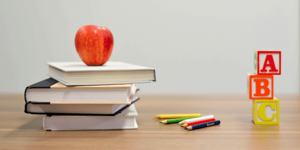 A stack of books with an apple on top, colouring pencils and A B C blocks on a table top