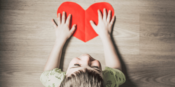 Small child laying on the floor with their hands on a red paper heart